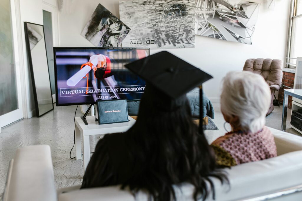 Two people watching a virtual graduation ceremony together at home, capturing the new normal of online celebrations.